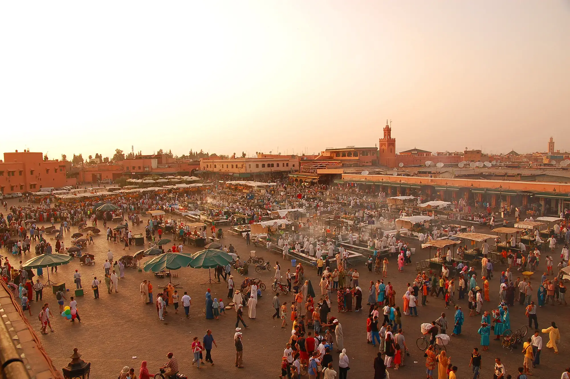 Jemaa el-Fna square at sunset, crowds and stalls, the Koutoubia minaret in the distance