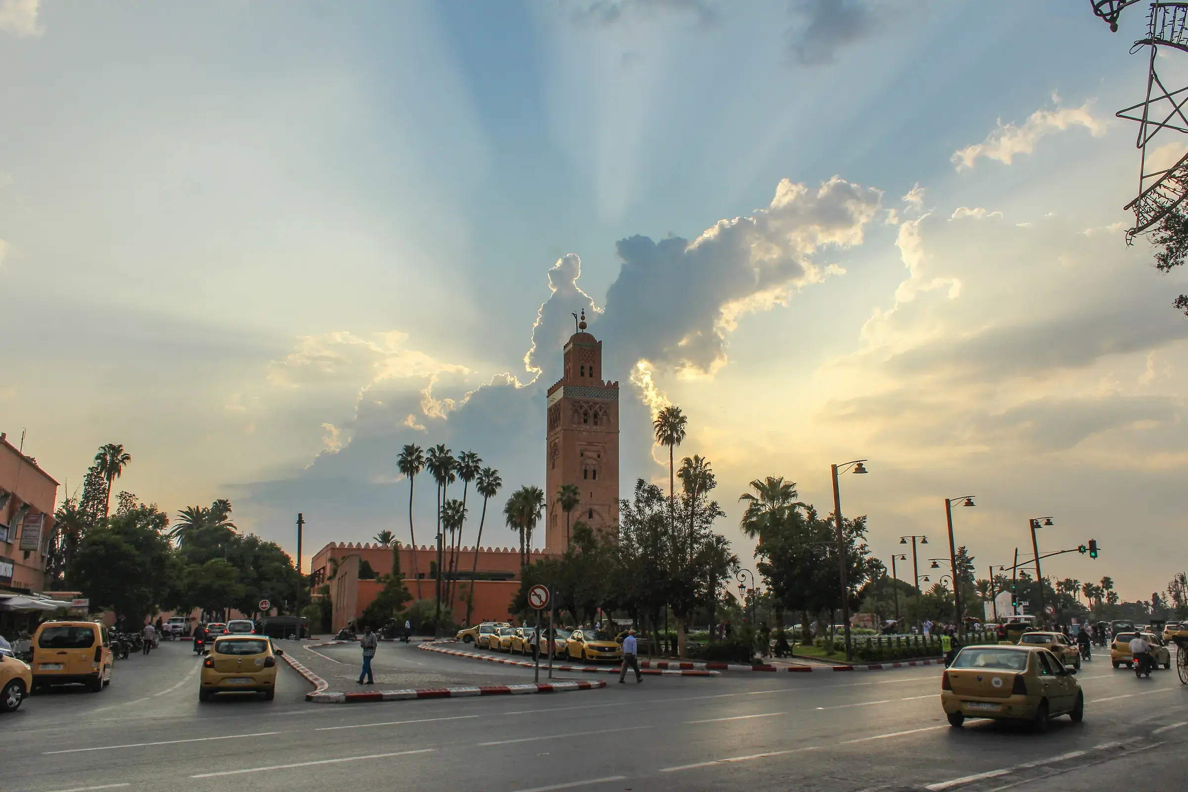 The Koutoubia minaret against a sunset sky streaked with rays, palm trees in the foreground