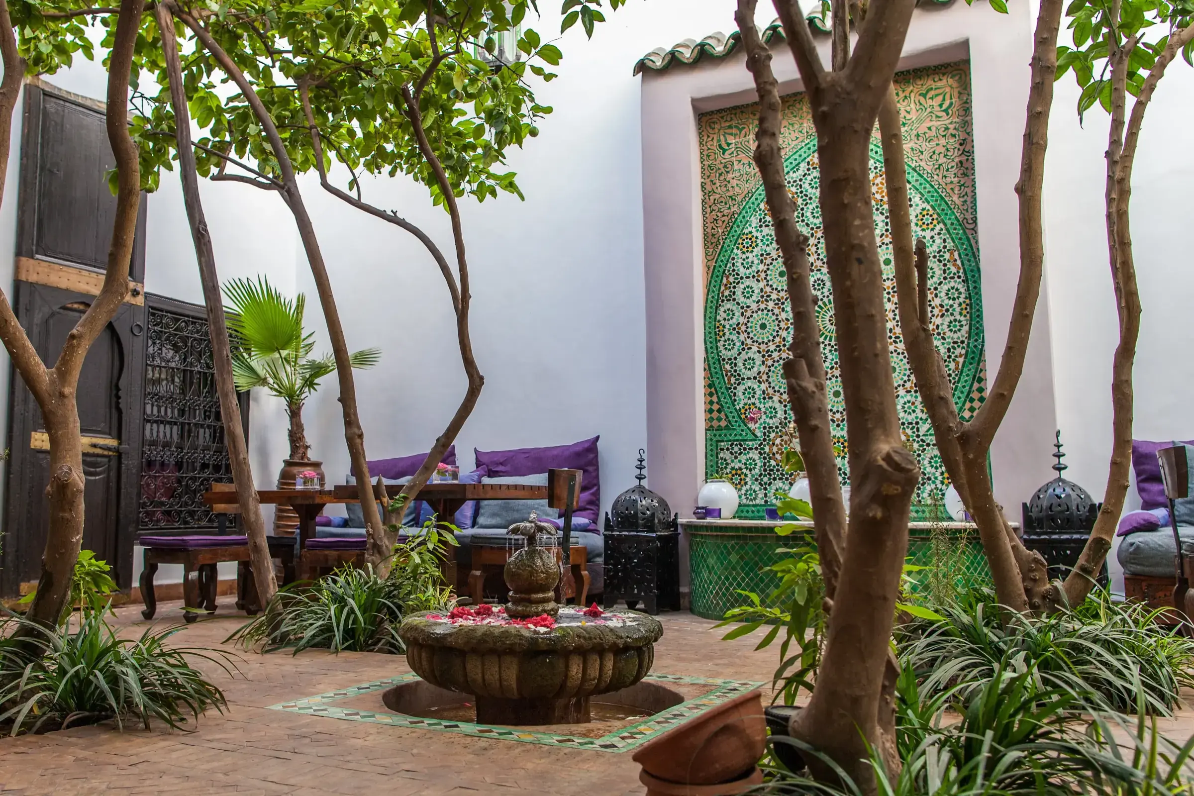 Patio de un riad de la medina de Marrakech: fuente, muro de zellige verde, naranjos y bancos a la sombra